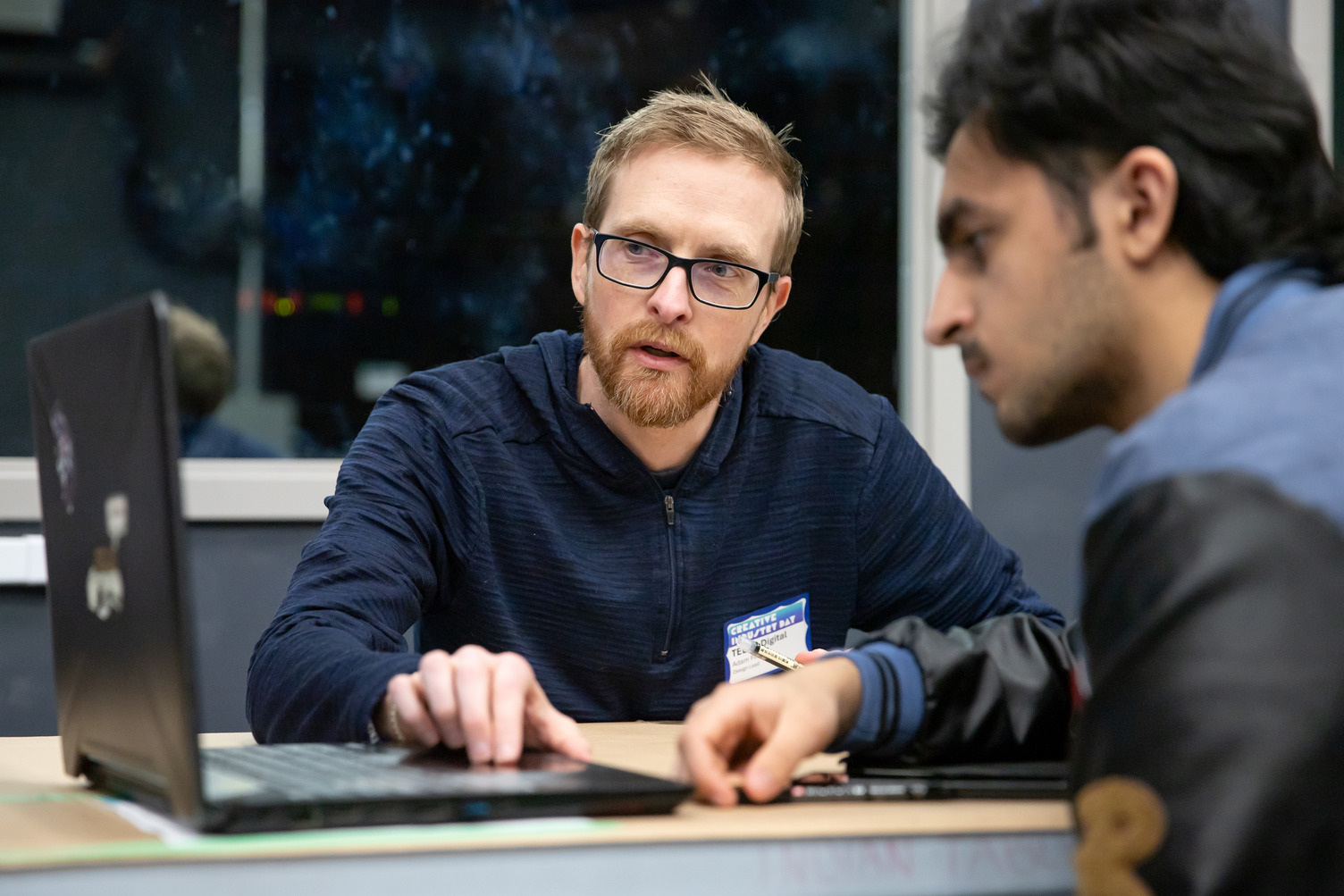 An industry lead and student look at a black laptop on the left