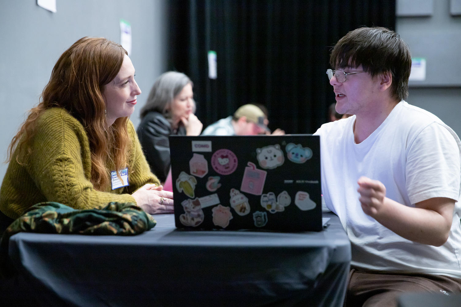 An industry lead and student look at a laptop with lots of stickers on it