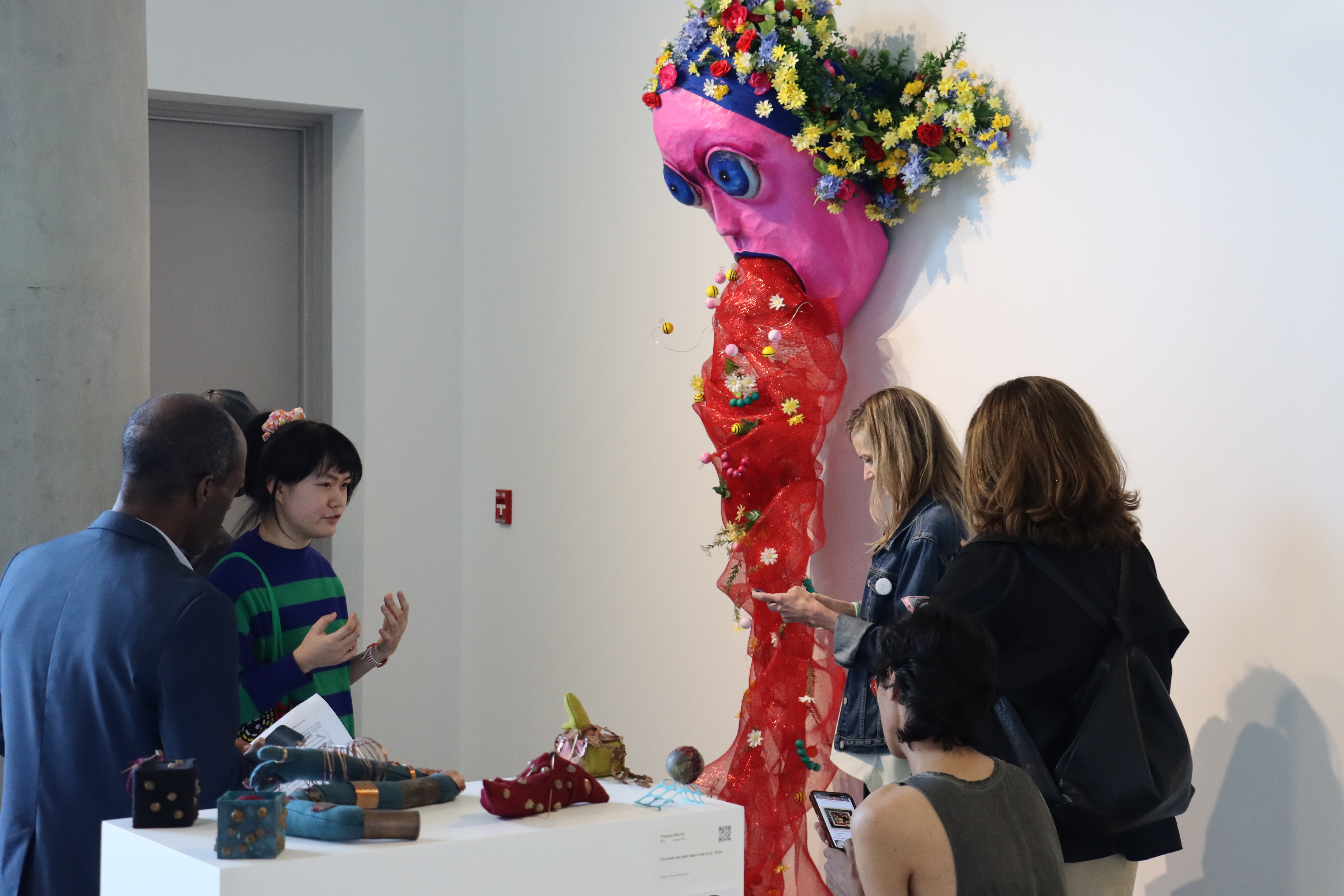 Four people surrounding a pink and red artwork that depicts a figure vomiting
