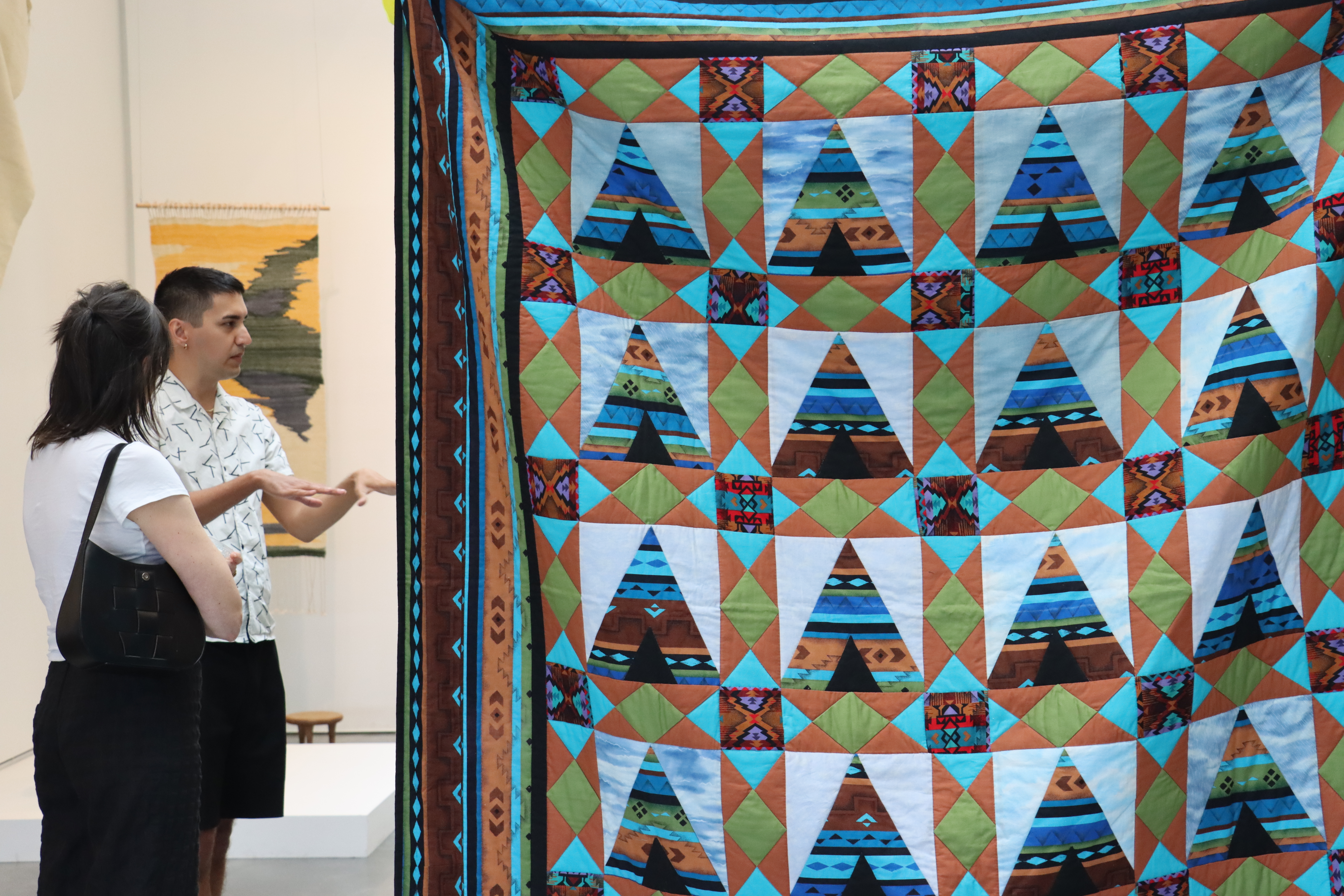Two people on the left in discussion with a blue and turquoise quilt in the foreground