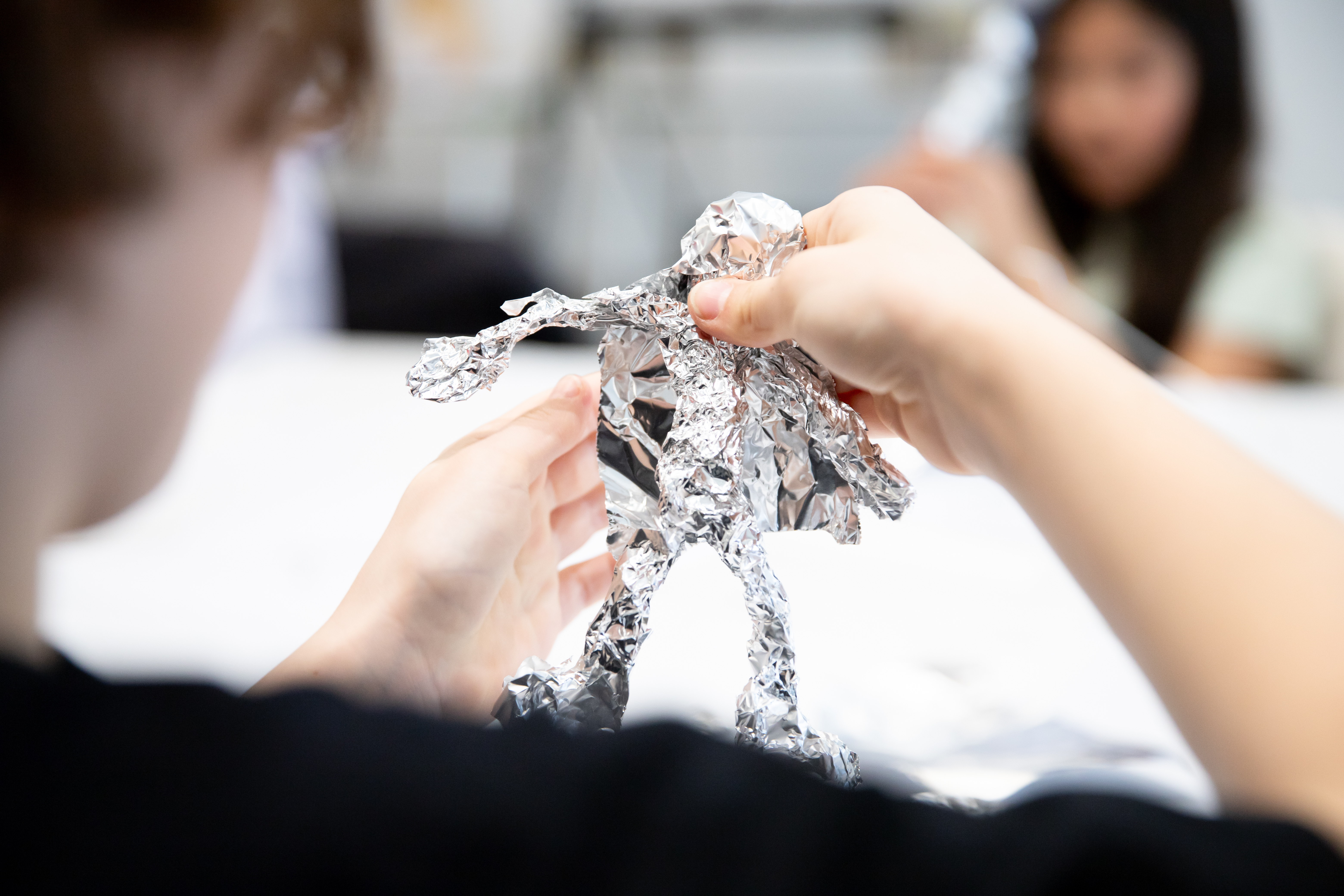Hands on a wiry figure with aluminum foil on it