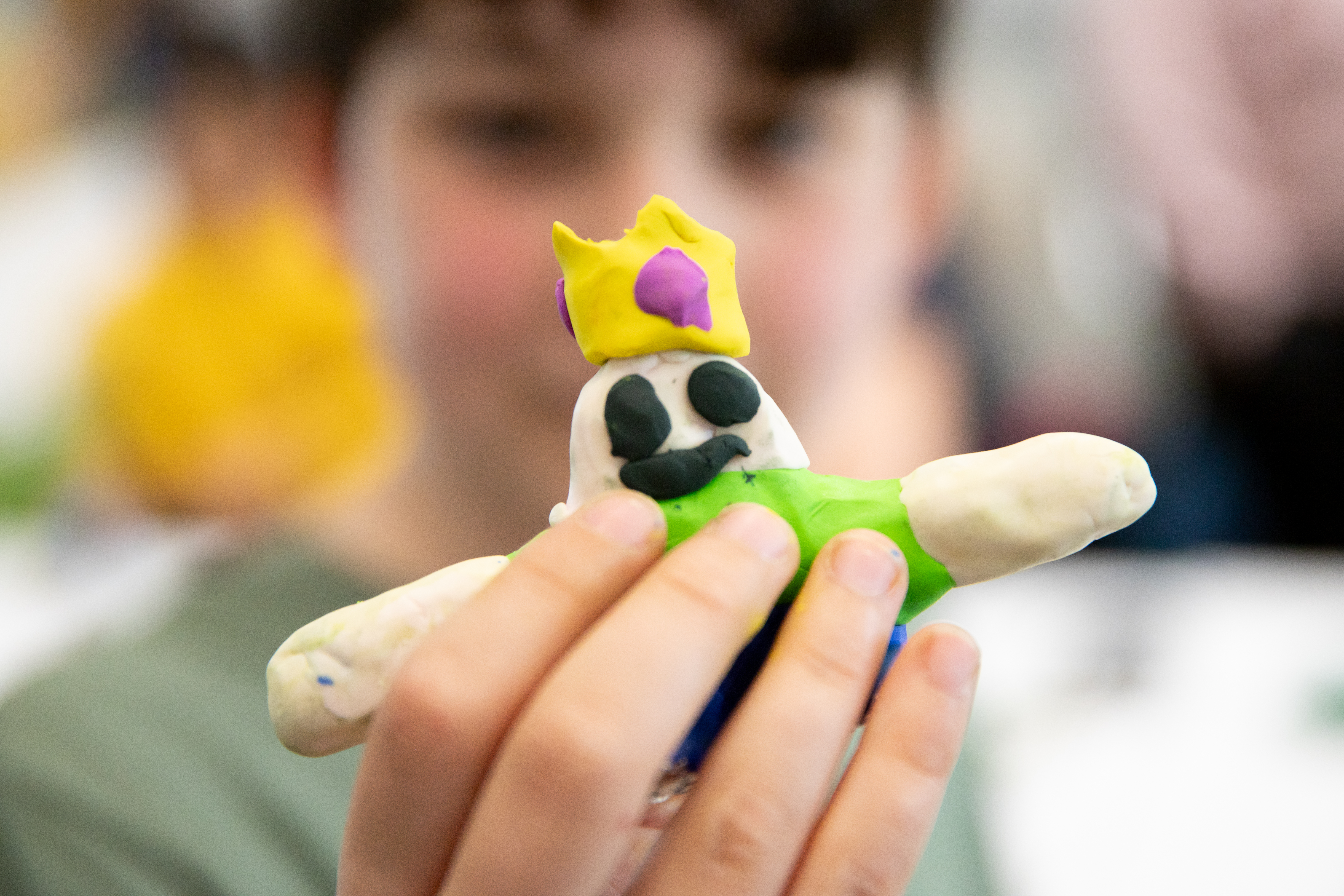Hands on a short plasticine figure with yellow crown, green shirt, and blue jeans