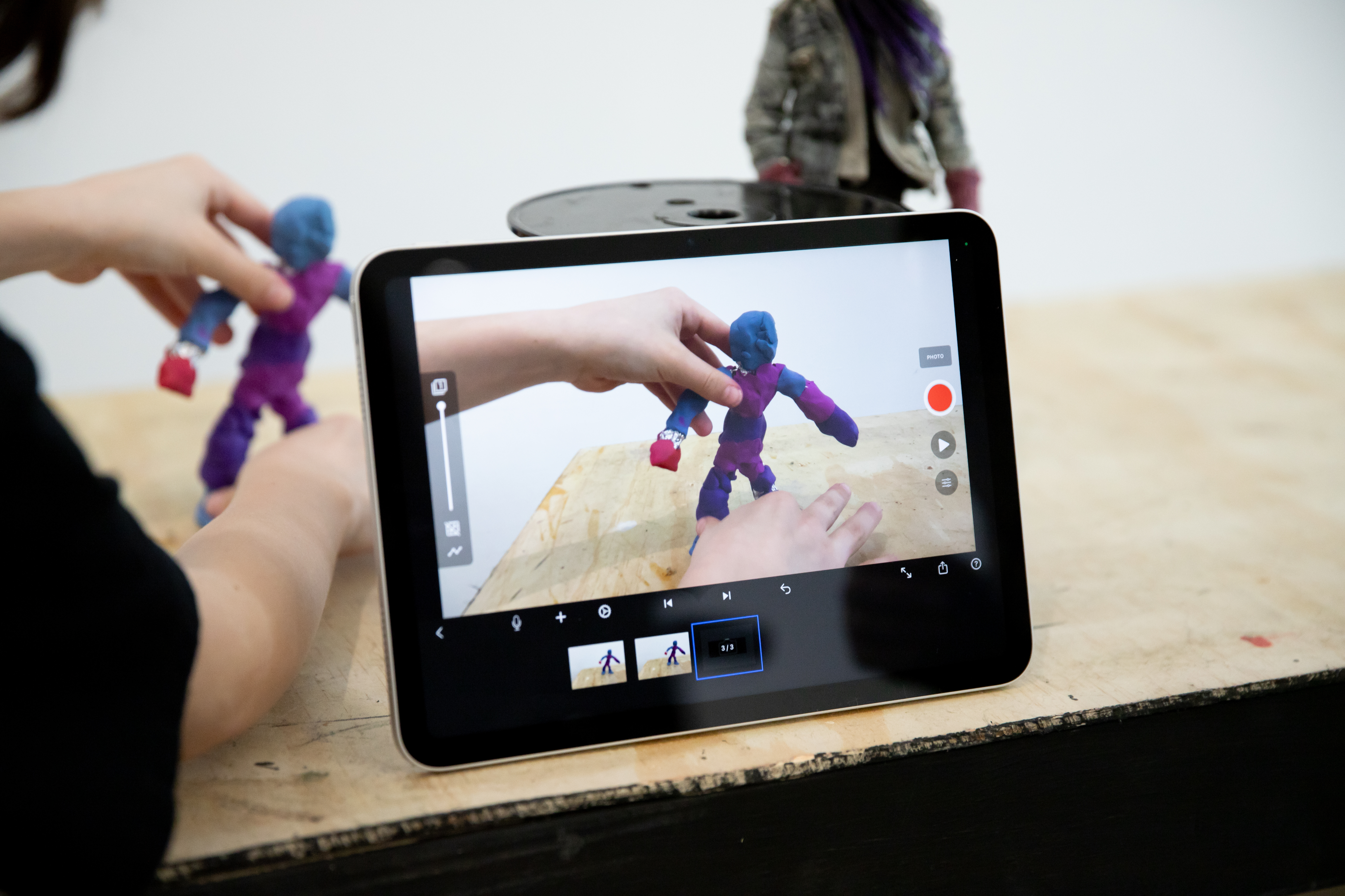 A student moves a blue-purple figure into frame with an iPad in the foreground