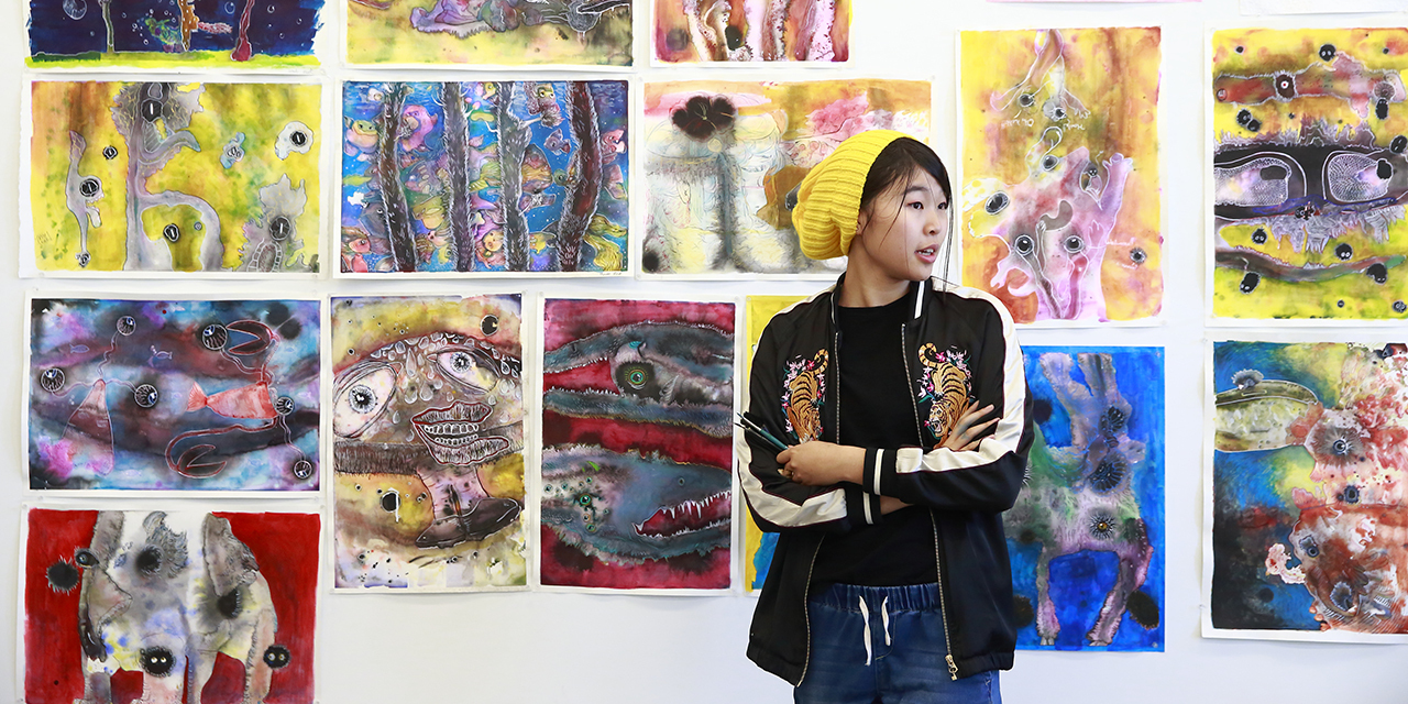 student in front of gallery wall full of drawings and paintings