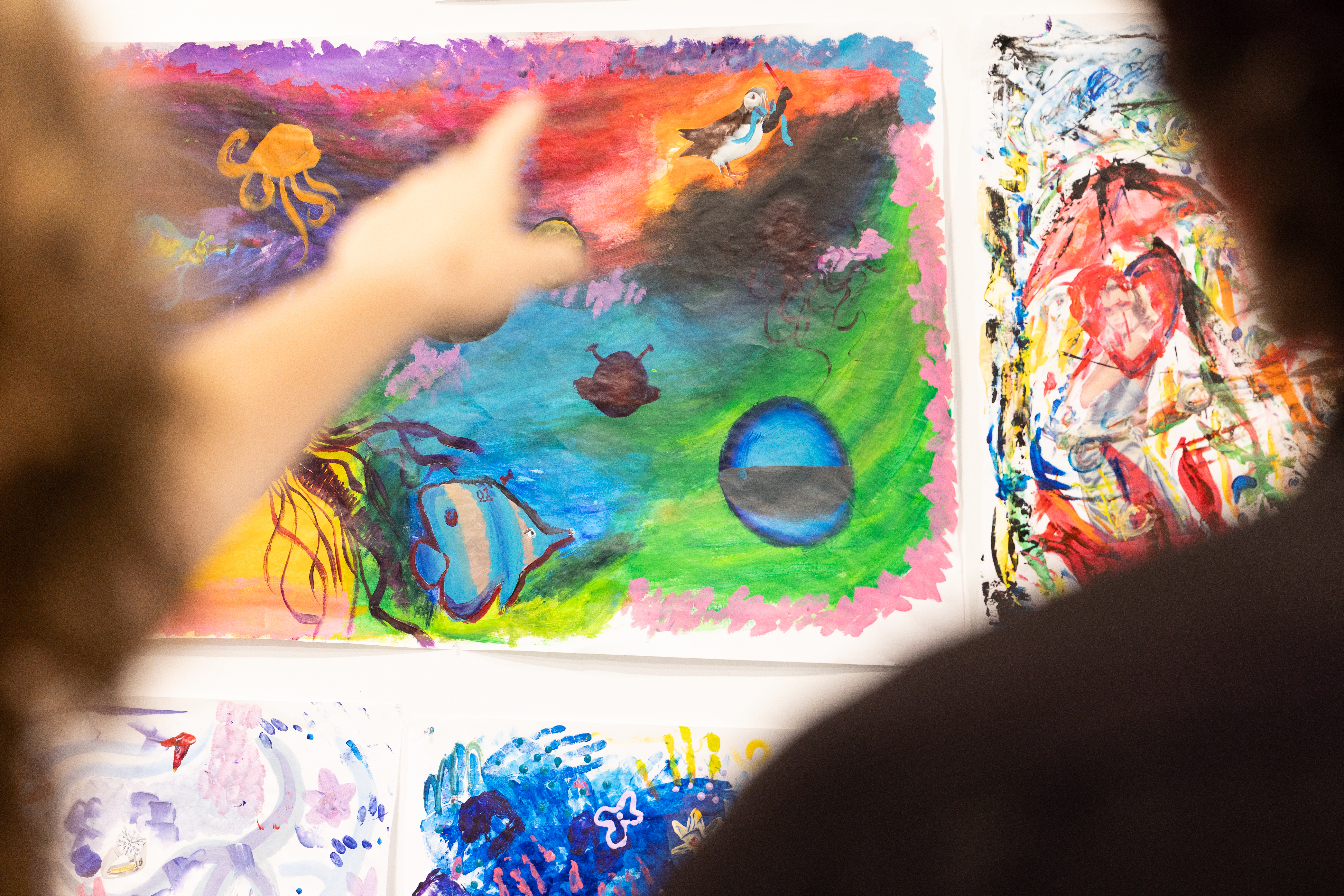 A person points out to an artwork with pink, yellow, green hues