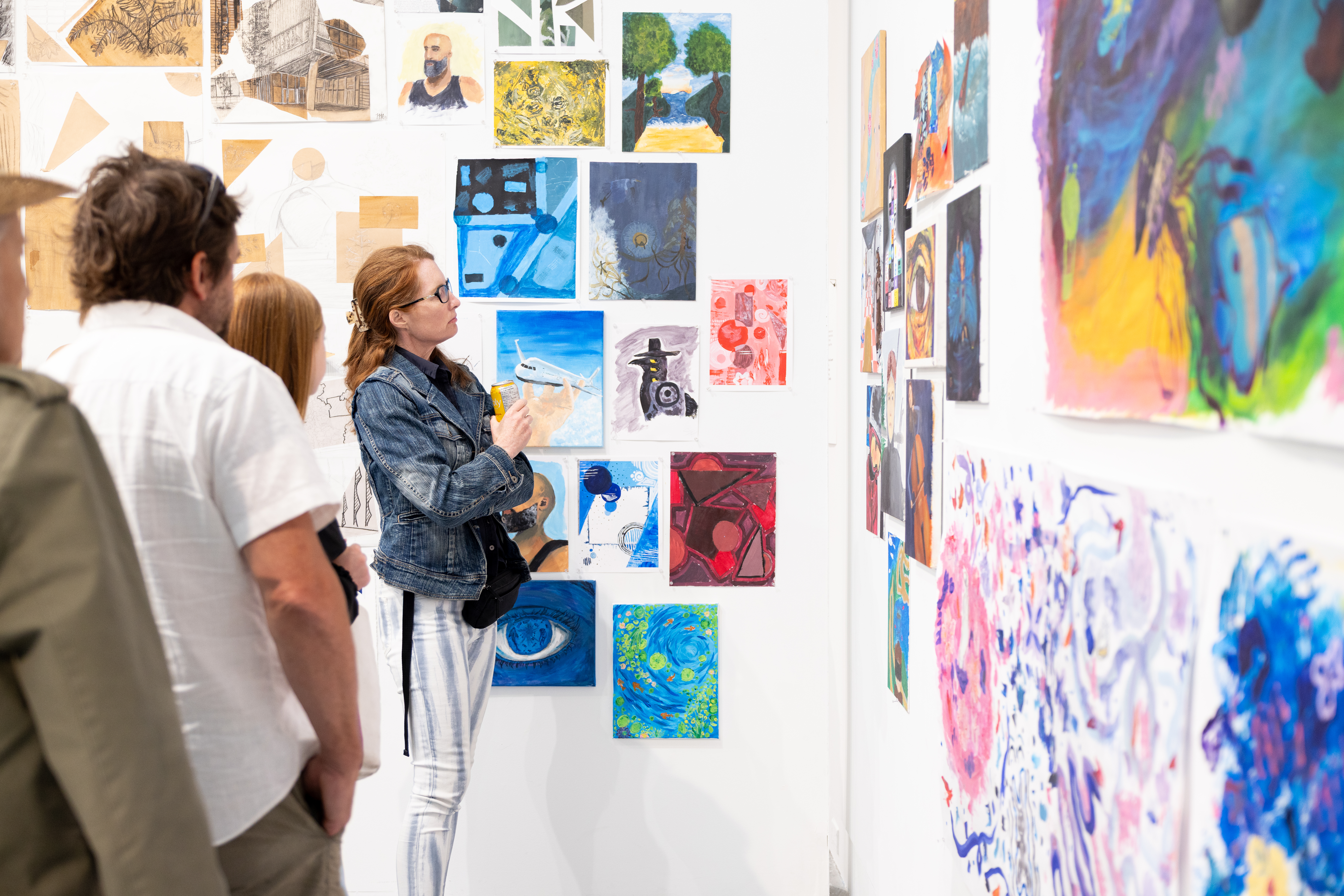 Three people on the left look at artworks on a wall with blue and green hues