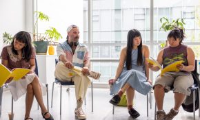 Four people sitting in chairs and some to the right are looking at a yellow book