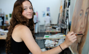 student painting looking at the camera smiling
