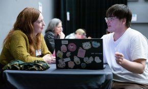 An industry lead and student look at a laptop with lots of stickers on it
