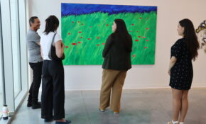 Four people surrounding an artwork with bright green, navy blue and red strokes