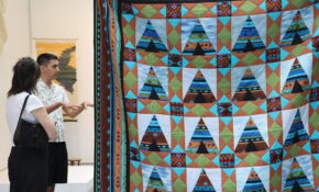 Two people on the left in discussion with a blue and turquoise quilt in the foreground