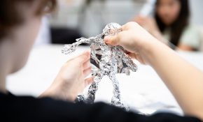 Hands on a wiry figure with aluminum foil on it