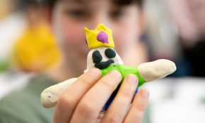 Hands on a short plasticine figure with yellow crown, green shirt, and blue jeans