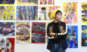 student in front of gallery wall full of drawings and paintings
