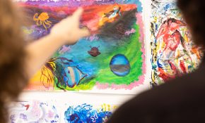 A person points out to an artwork with pink, yellow, green hues