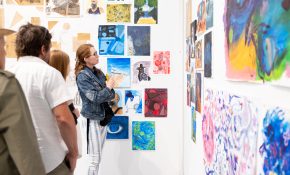 Three people on the left look at artworks on a wall with blue and green hues