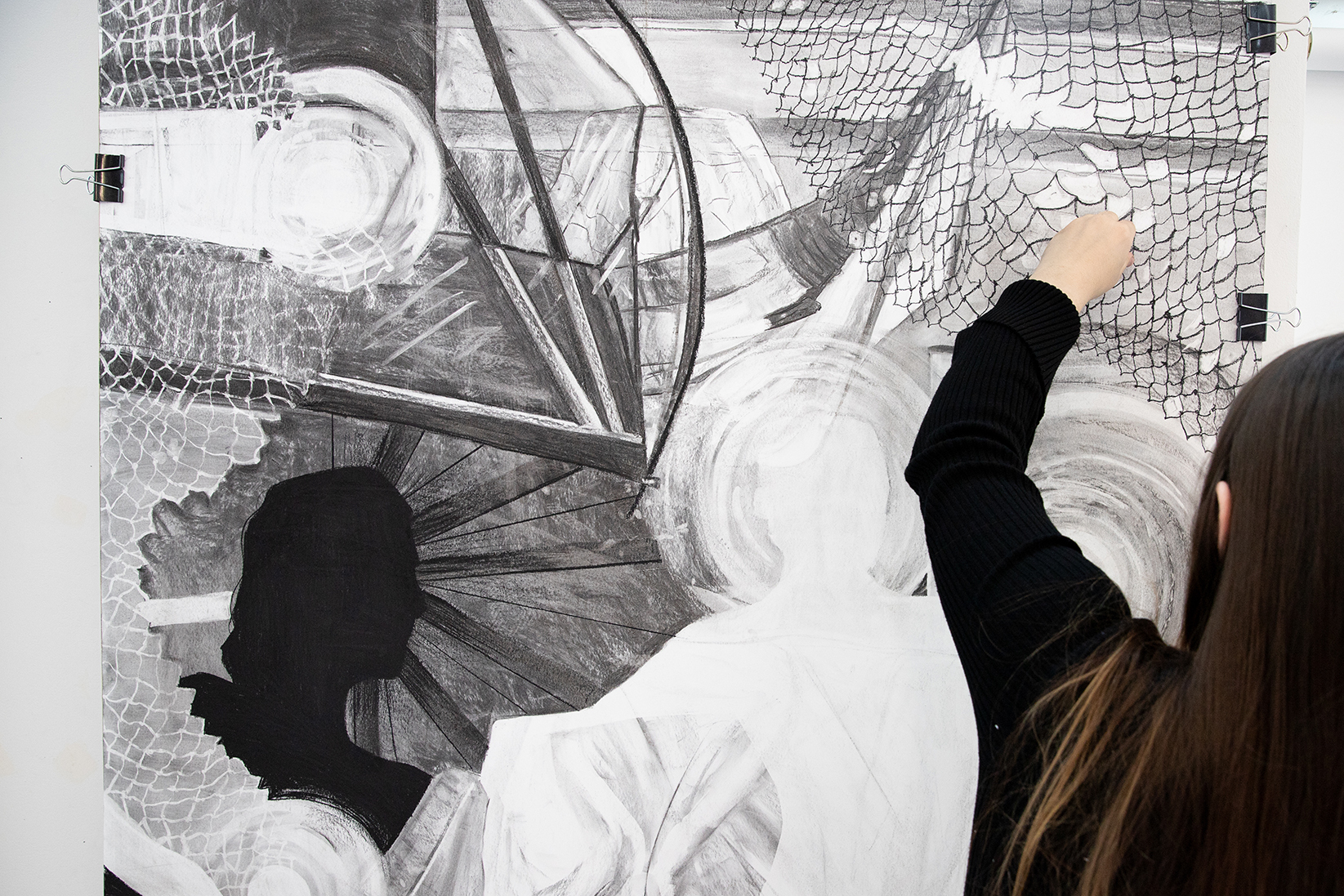A person with long hair and a black shirt works on a black-and-white drawing.