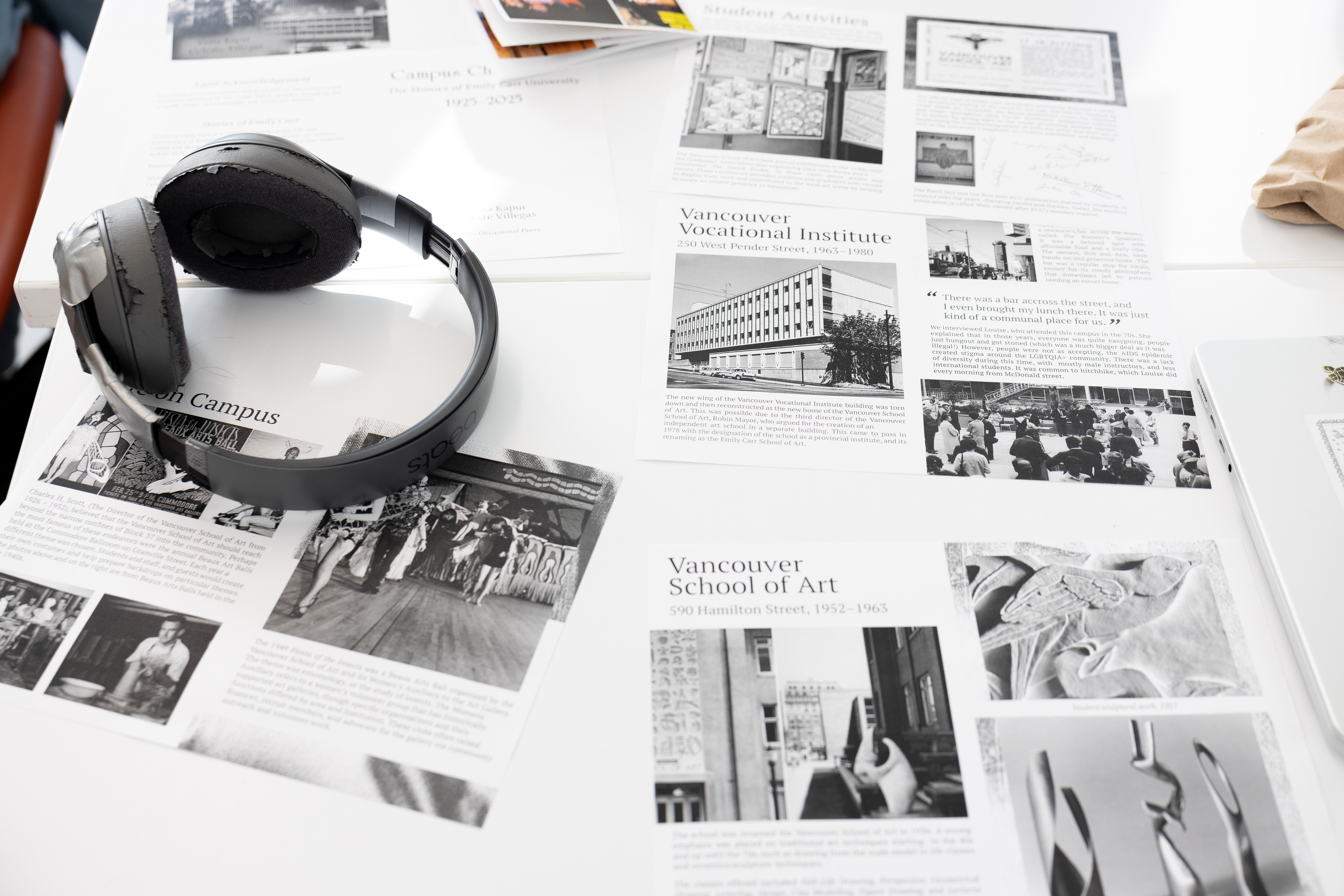 Pieces of paper bearing black and grey text and graphics are spread across a table underneath a pair of over-ear headphones on the left side of the image.