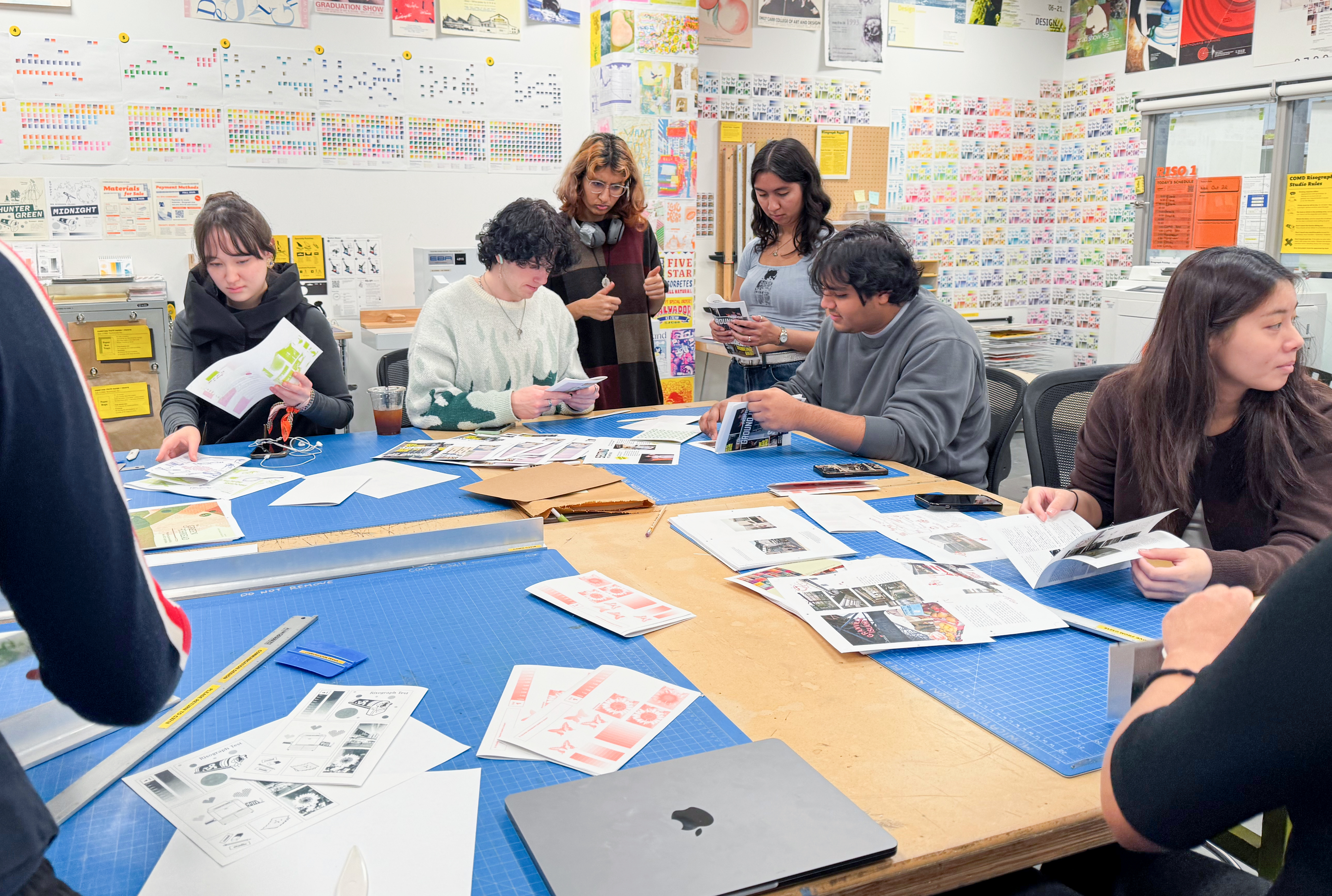People work with printed publications around a table in a studio bearing colourful risograph prints on the walls.