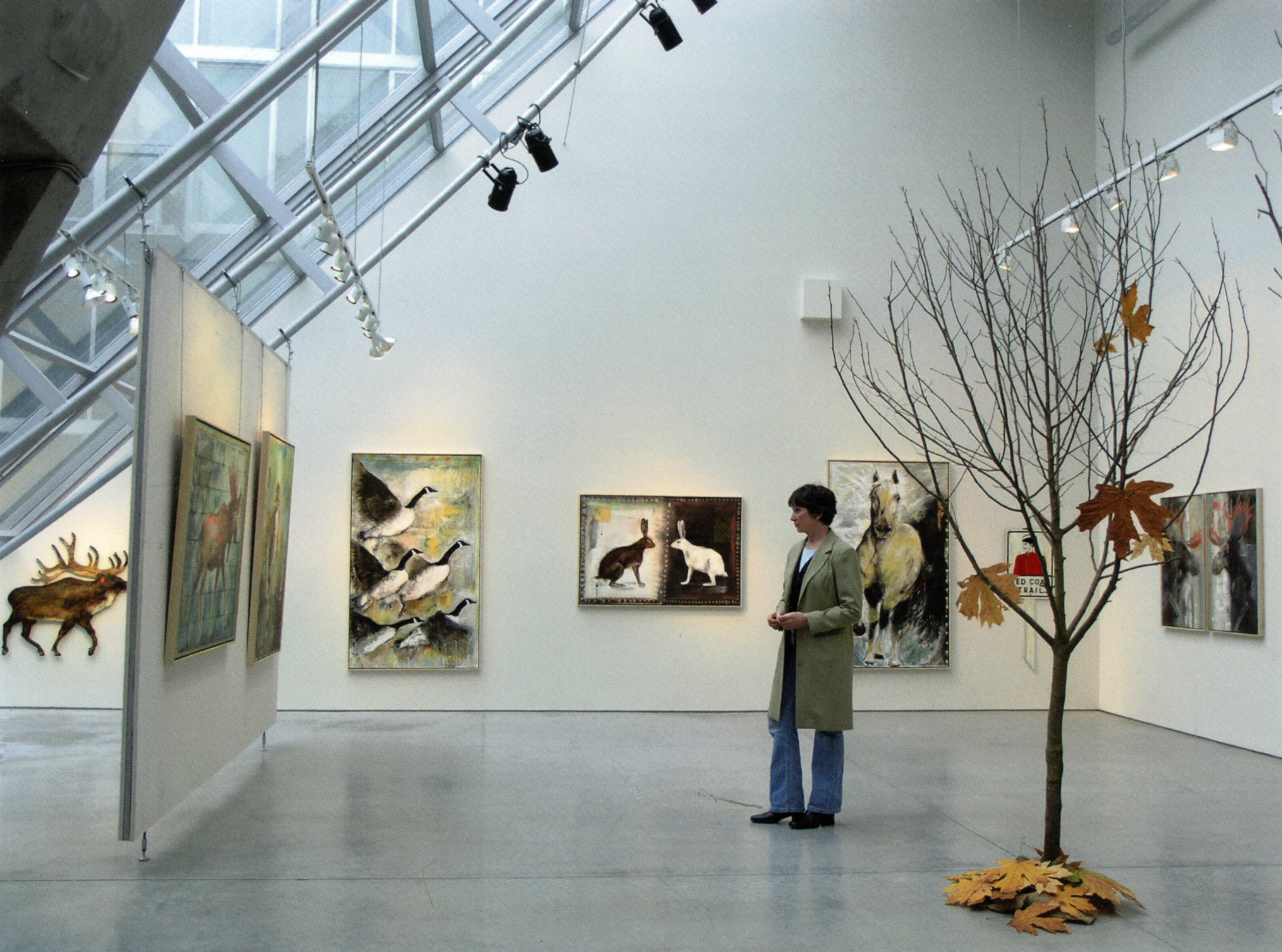 Artist viewing animal-themed paintings in a bright gallery space with angled skylights.