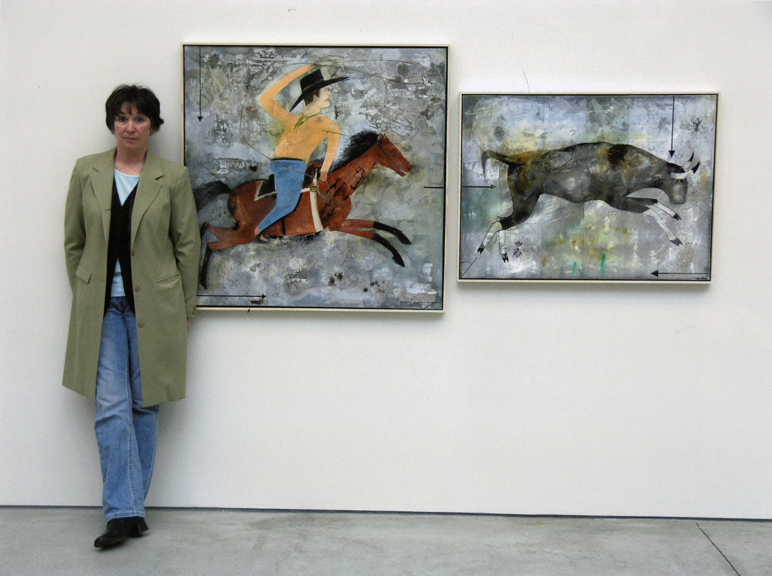 Artist standing beside two paintings depicting a rider on horseback and a running bull.
