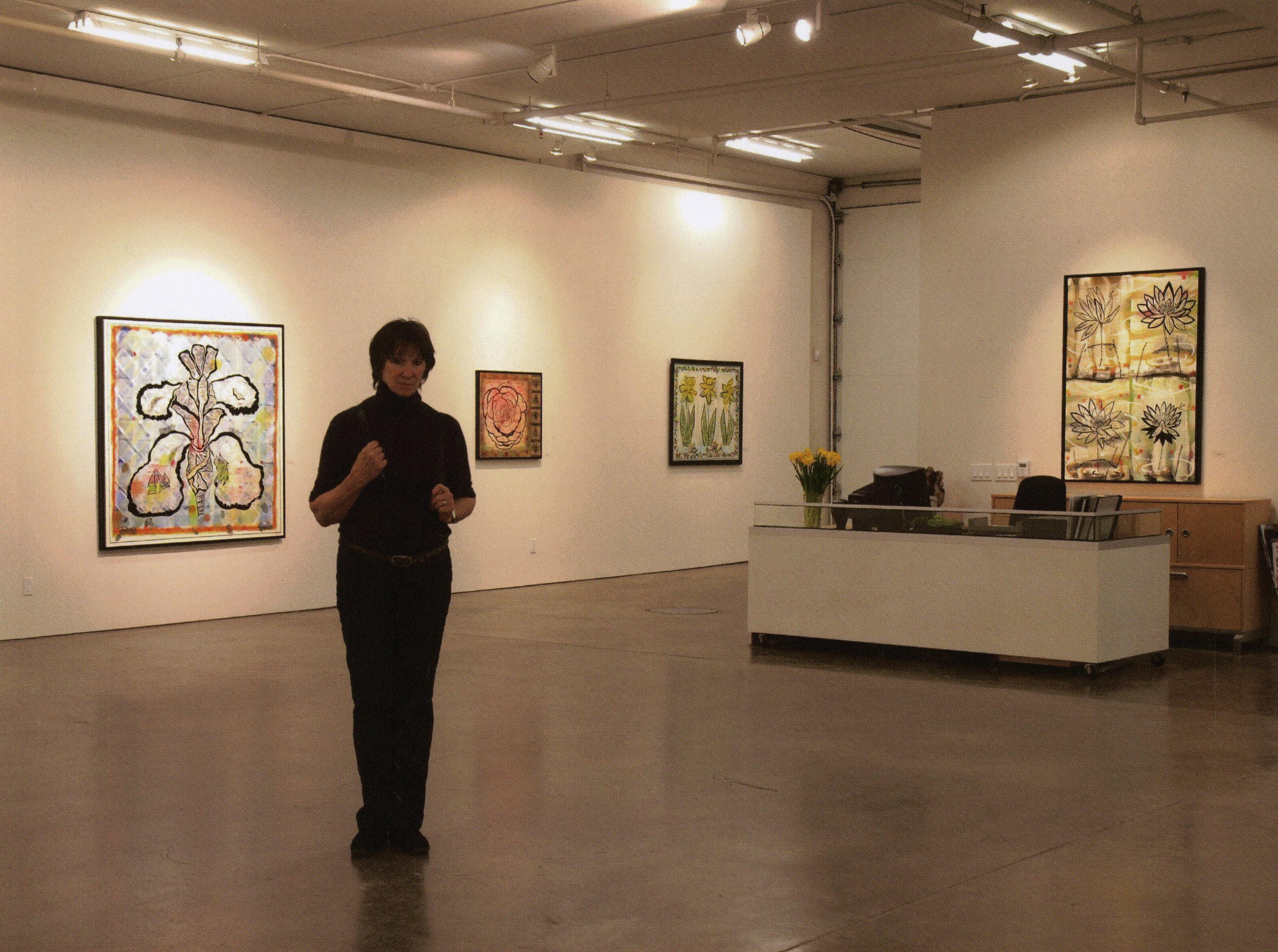 Artist standing in a gallery surrounded by floral paintings and warm lighting.