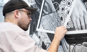 A person works in close-up on a large-scale black-and-white drawing.