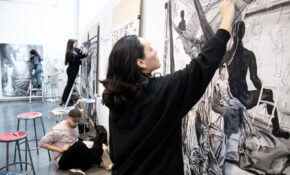 A group of students in a large studio work at the same time on separate, large-scale drawings.