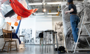 A still-life comprising furniture, netting and drapery hangs in a studio amidst a group of artists working on drawings.