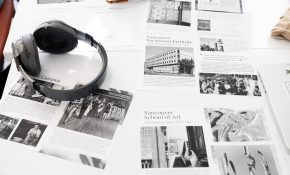 Pieces of paper bearing black and grey text and graphics are spread across a table underneath a pair of over-ear headphones on the left side of the image.