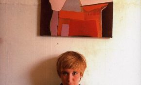 Young Janey Adams with short blonde hair, against a white wall with an abstract painting hanging overhead