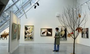 Artist viewing animal-themed paintings in a bright gallery space with angled skylights.