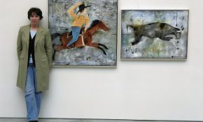 Artist standing beside two paintings depicting a rider on horseback and a running bull.
