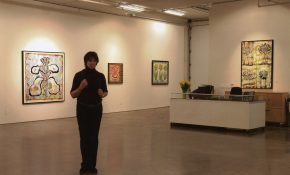 Artist standing in a gallery surrounded by floral paintings and warm lighting.