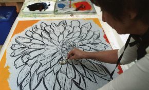 Artist using a spoon to burnish a large black-and-white flower print on a bright orange background.